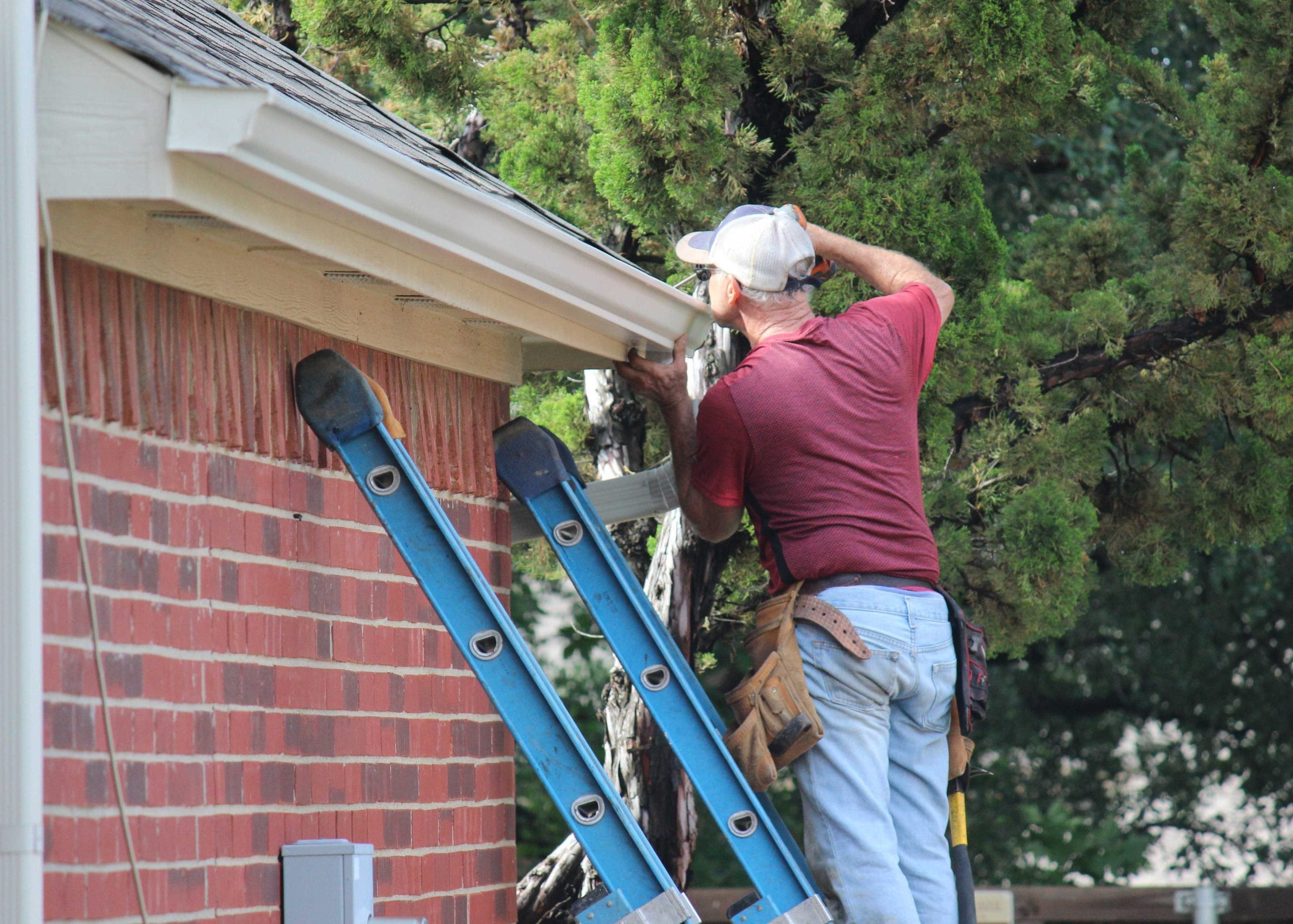 A professional emergency roof repair contractor wears grey hat on ladder in Whittier, California